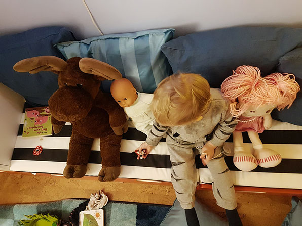 Kleinkind spielt mit Puppen und Kuscheltieren. In der Zeit kann Mama sich etwas vom Alltags-Stress erholen.